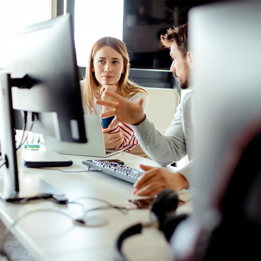 Two people discuss Cloud Analytics at their desks; one gestures while the other listens intently to new insights.