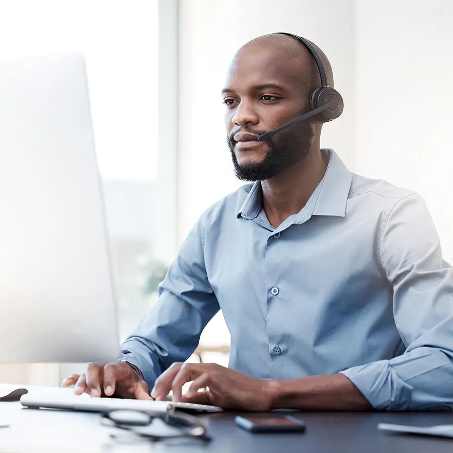 Man wearing headset at desk, typing and working on adjudication in a bright office environment.