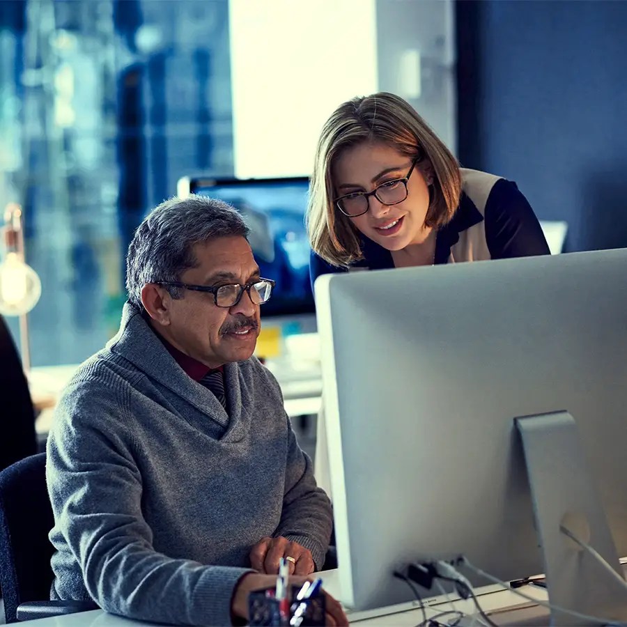 Two colleagues wearing glasses review Analytics-as-a-Service data on a large monitor in a modern, well-lit office.