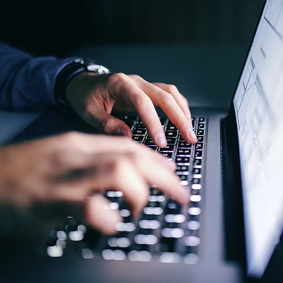 Close-up of hands typing on a laptop, managing Enrollment and Billing Services in a dimly lit setting.