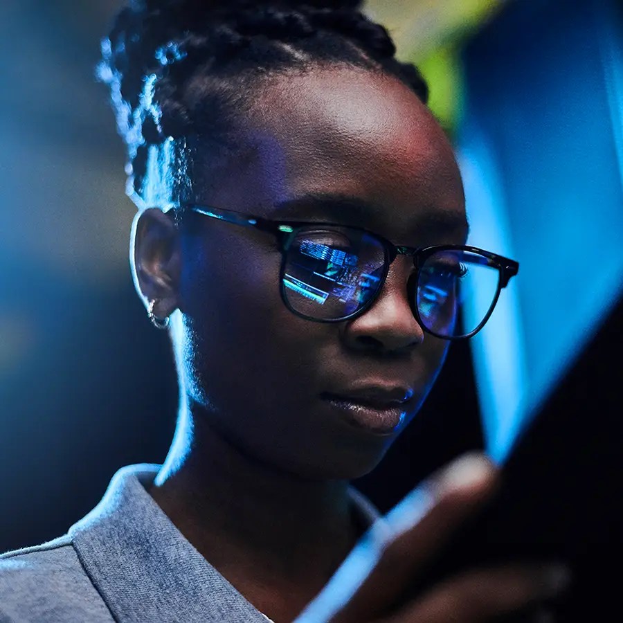 A woman wearing glasses studies a tablet, blue light reflected on her lenses—exploring Customer Touchpoint Analytics.