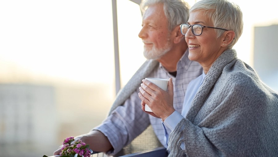 Smiling older couple with gray hair enjoy coffee and flowers on a balcony, reflecting on stabilizing nursing workforce efforts.