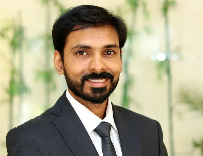Man with short black hair and beard in a dark suit, smiling, ready to orchestrate intelligent operations for your team.