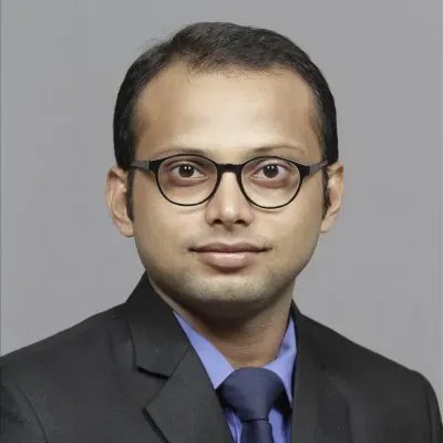 A man with short hair, glasses, and a suit poses for a professional headshot, ready to orchestrate intelligent operations.