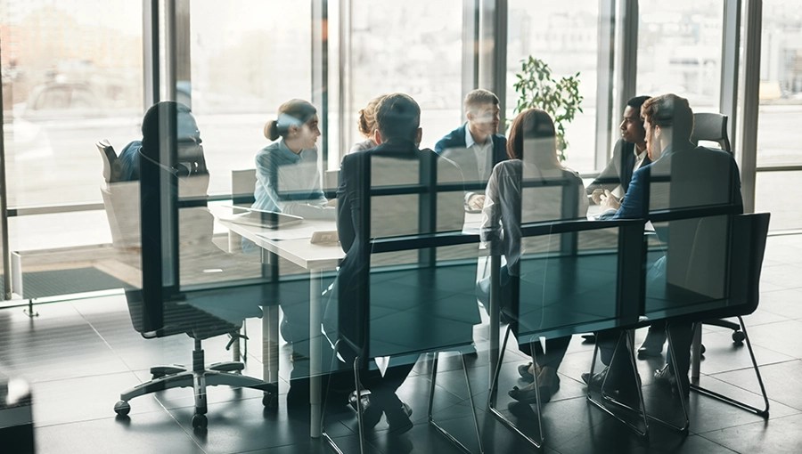 Eight people discuss the operational advantage of IDR changes around a sunlit conference table in a modern office.