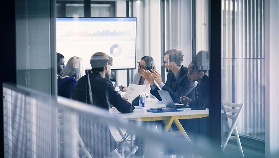 Six businesspeople discuss documents and charts, focusing on improving payment accuracy in a glass-walled office.