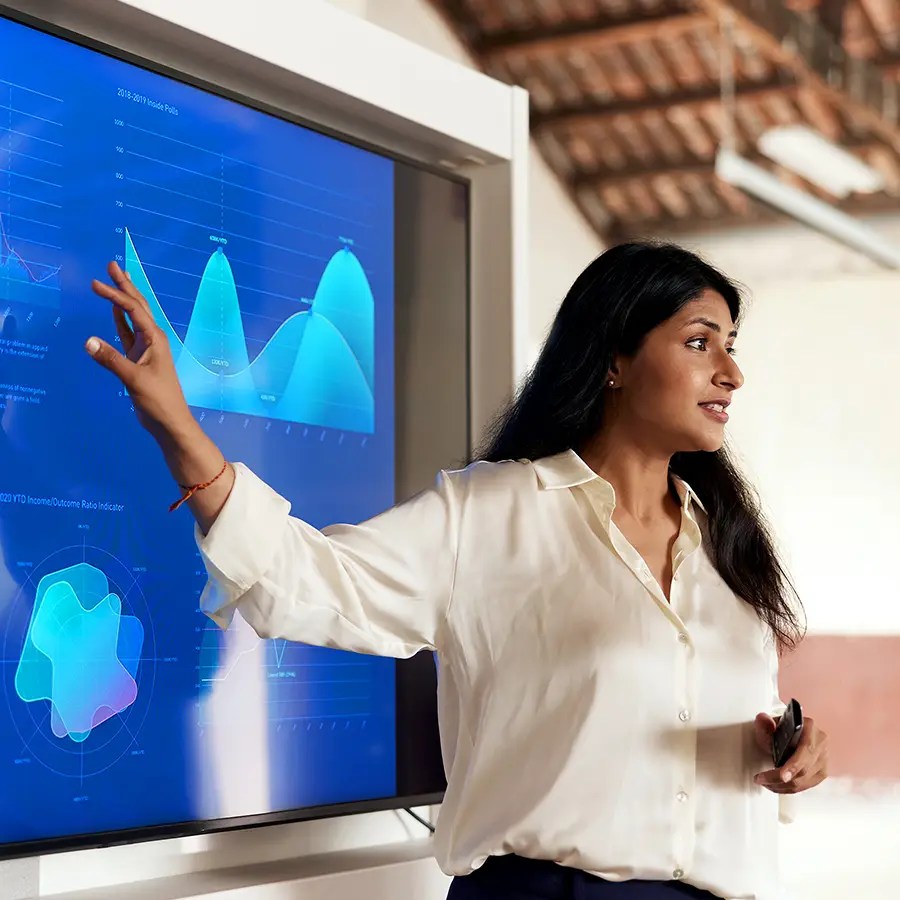 Woman in white blouse gestures at data charts, leading a Provider Operations meeting in a room with exposed beam ceiling.
