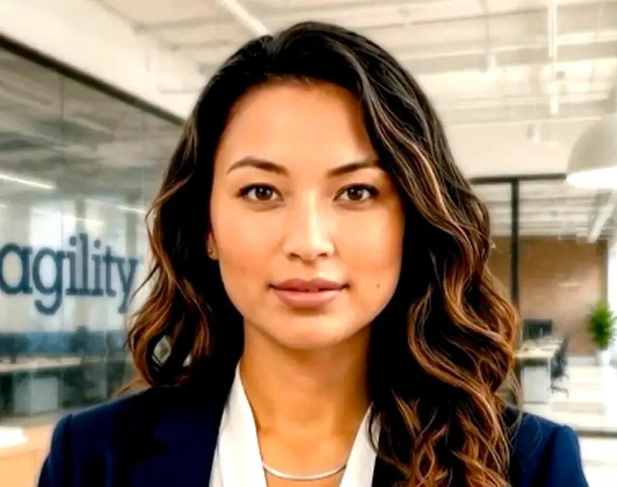 A woman with long wavy hair stands in an office, wearing a blazer. Agility is visible on the glass wall behind her.