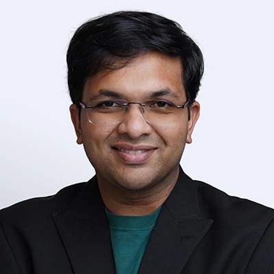 Smiling man with short dark hair, glasses, and a black blazer over green shirt, embodying enterprise intelligence.