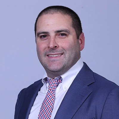 Smiling man in a blue suit, embodying enterprise intelligence, stands against a plain light background.