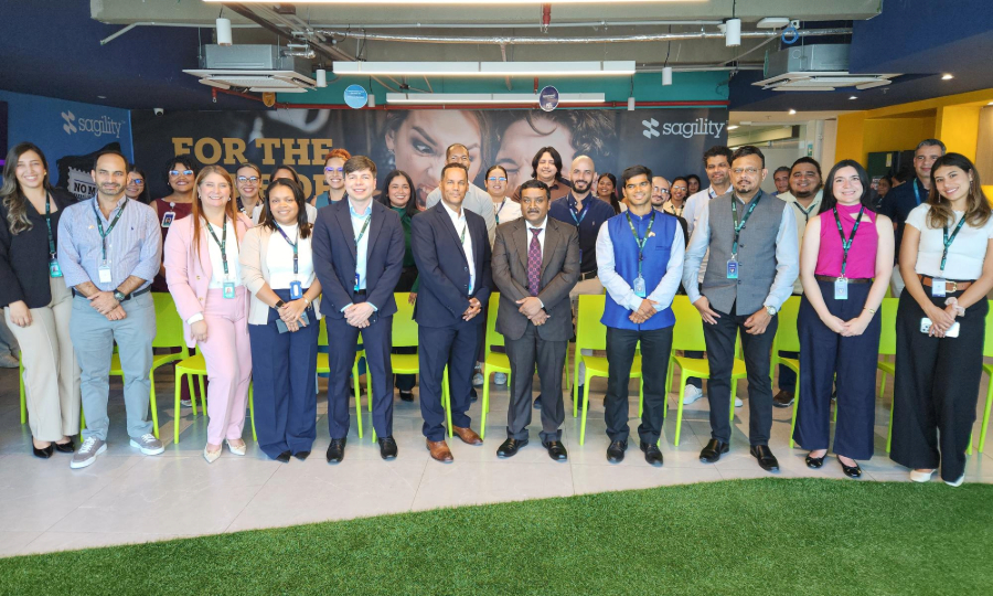 A diverse group of Sagility colleagues stand together for a photo in an office with a green turf floor.